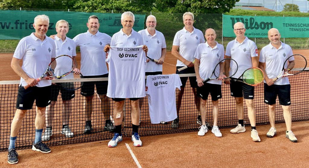 Neun Tennisspieler der Herren-50-Mannschaft der TASF Gechingen stehen lächelnd am Netz eines Sandplatzes in einheitlichen weißen Poloshirts mit Vereinslogo und schwarzen Shorts. Zwei von ihnen halten je ein weißes T-Shirt mit der Aufschrift „TASF Gechingen" und dem DVAG-Logo samt Schriftzug „Jürgen Weber" in die Kamera. Im Hintergrund sind Werbebanden, ein Maschendrahtzaun und grüne Bäume zu sehen.